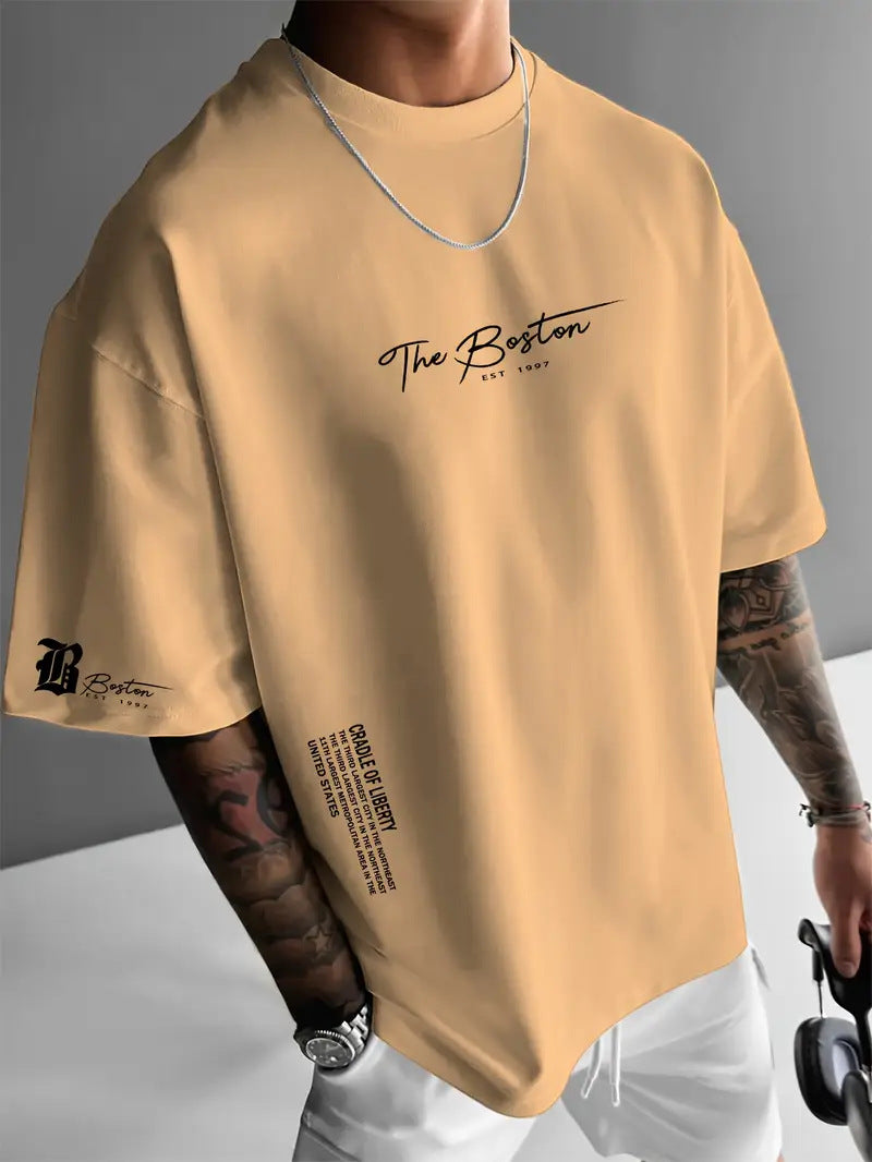 Tan oversized t-shirt with a script print on the chest and a small sleeve emblem, worn by a model, front view