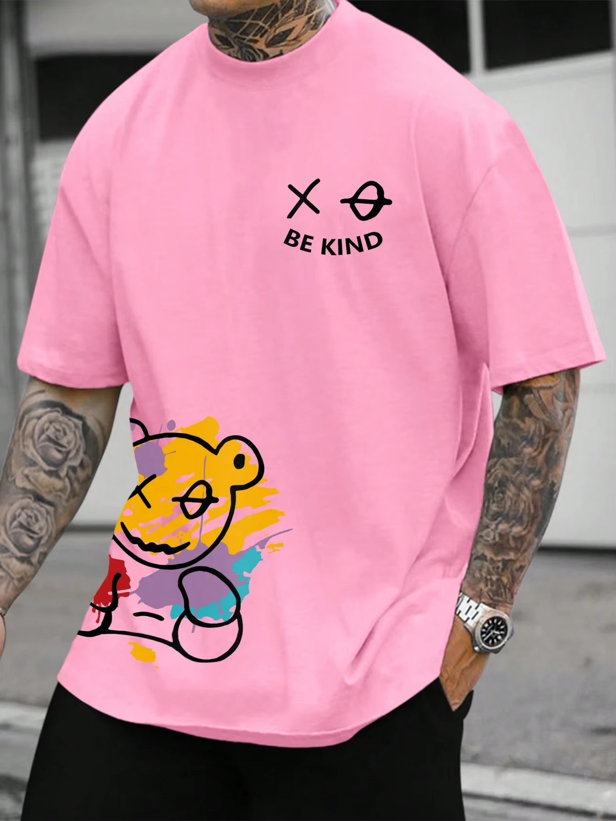 Pink t-shirt with a cartoon bear graphic at the hem and small text on the chest, worn by a model, front view